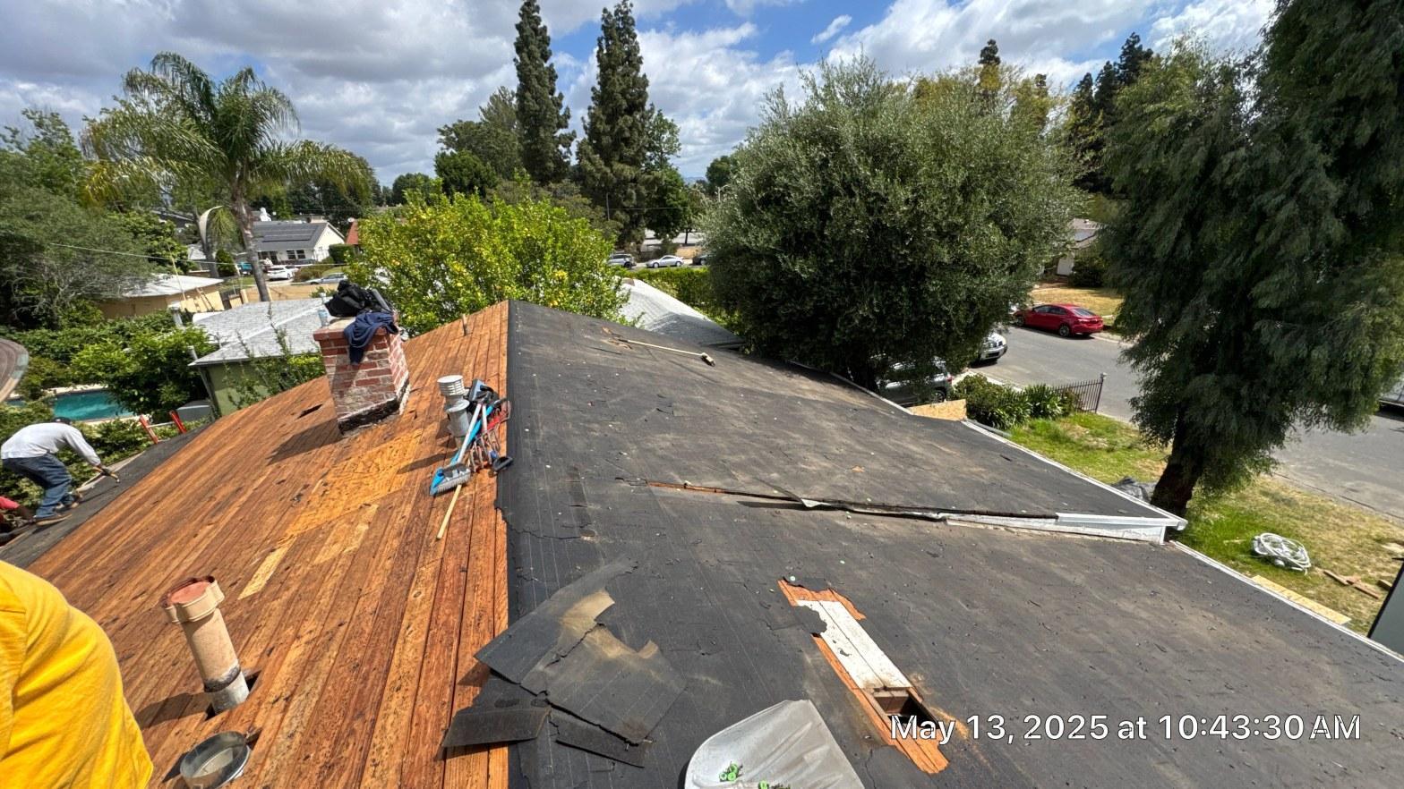 shingle-reroof-6643-saloma-ave-los-angeles-675 Roofing tear-off in progress showing exposed wood sheathing, brick chimney, and partial old felt underlayment on house.