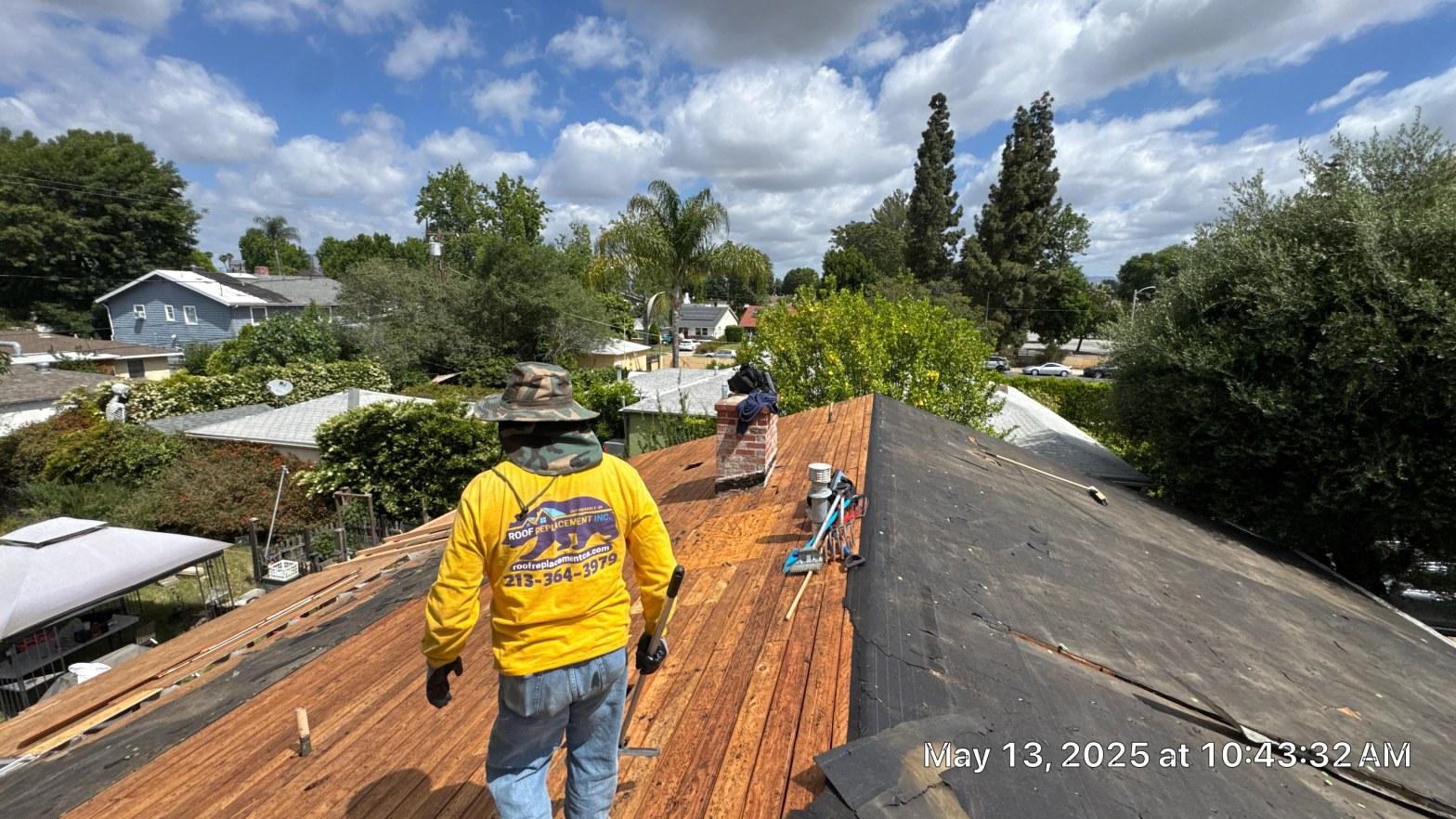 shingle-reroof-6643-saloma-ave-los-angeles-676 Roof Replacement Inc. worker in yellow shirt removing old shingles, exposing wood decking on residential roof, Los Angeles.