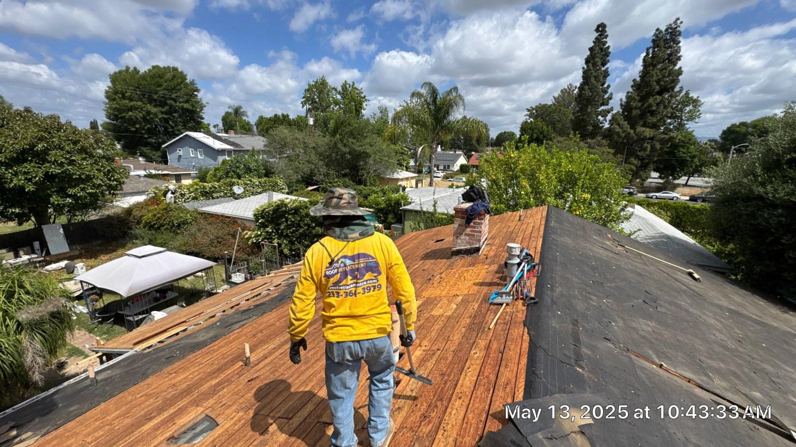 shingle-reroof-6643-saloma-ave-los-angeles-679 Roof Replacement Inc. worker in yellow shirt stripping old shingles, exposing wood decking on residential home.