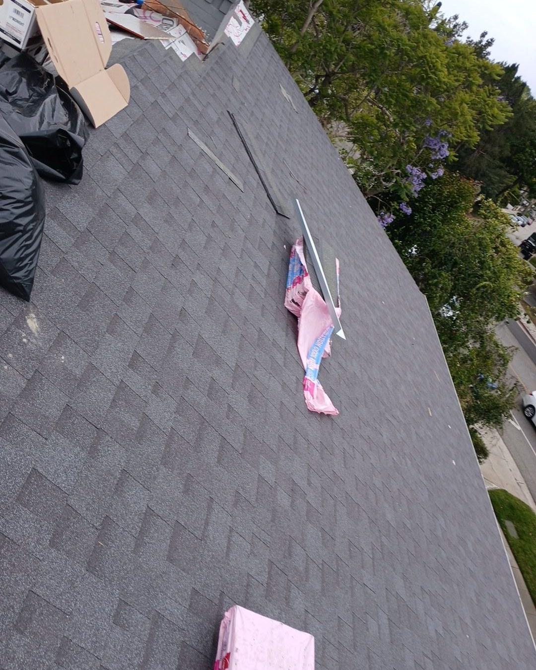 shingle-reroof-motor-ave-los-angeles-605 Freshly installed gray architectural asphalt shingles on residential roof slope with pink insulation and cardboard debris on surface.