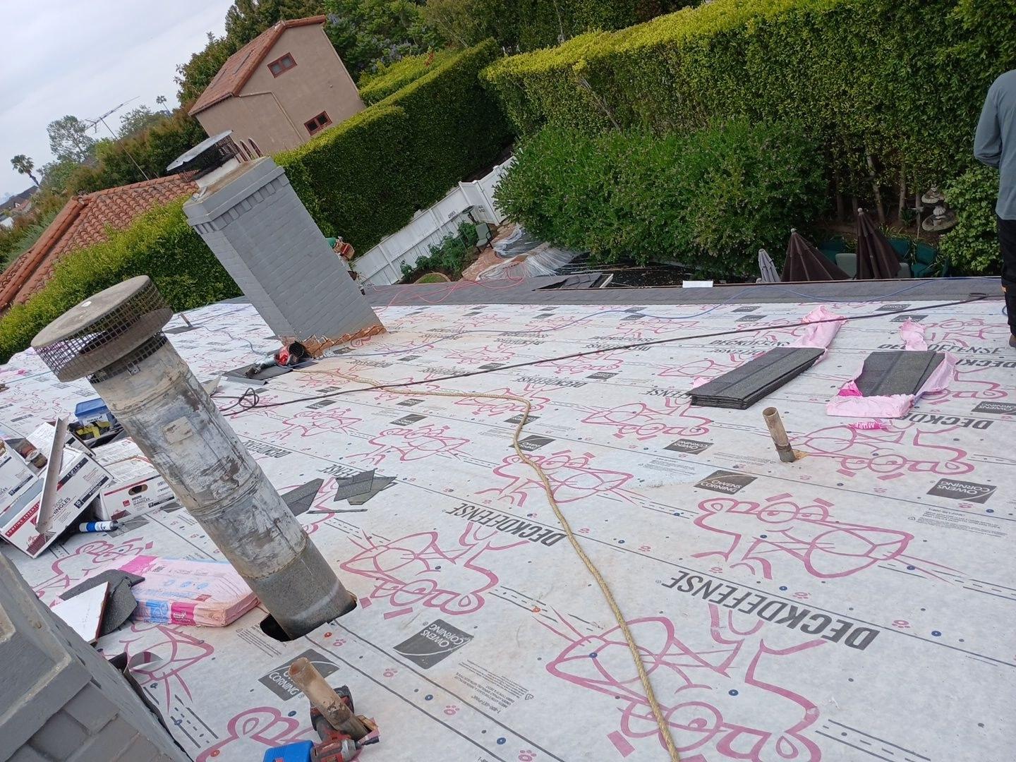 shingle-reroof-motor-ave-los-angeles-606 Residential roof mid-replacement showing Owens Corning DeckDefense underlayment, chimney, pipe penetrations, and scattered shingles.
