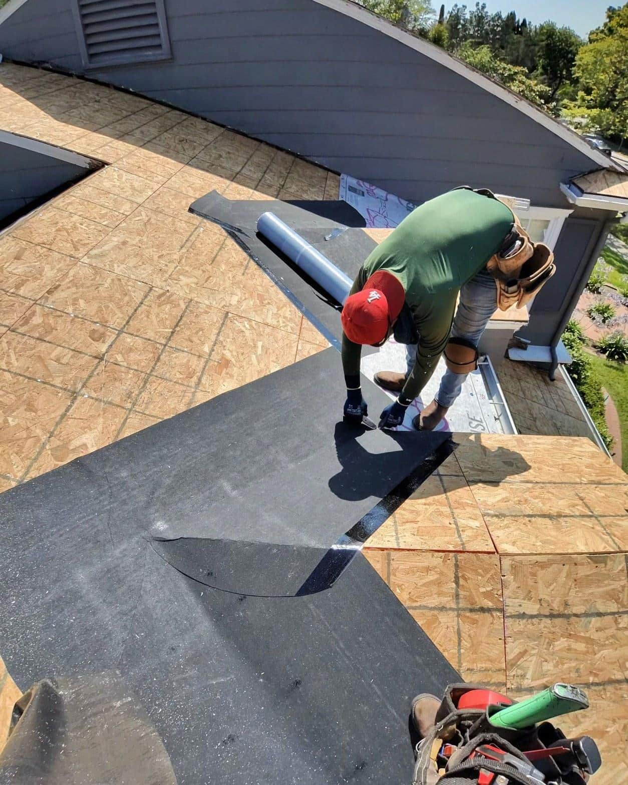 shingle-reroof-motor-ave-los-angeles-607 Roofer in red cap rolling out black felt underlayment on OSB sheathing during residential roof replacement.