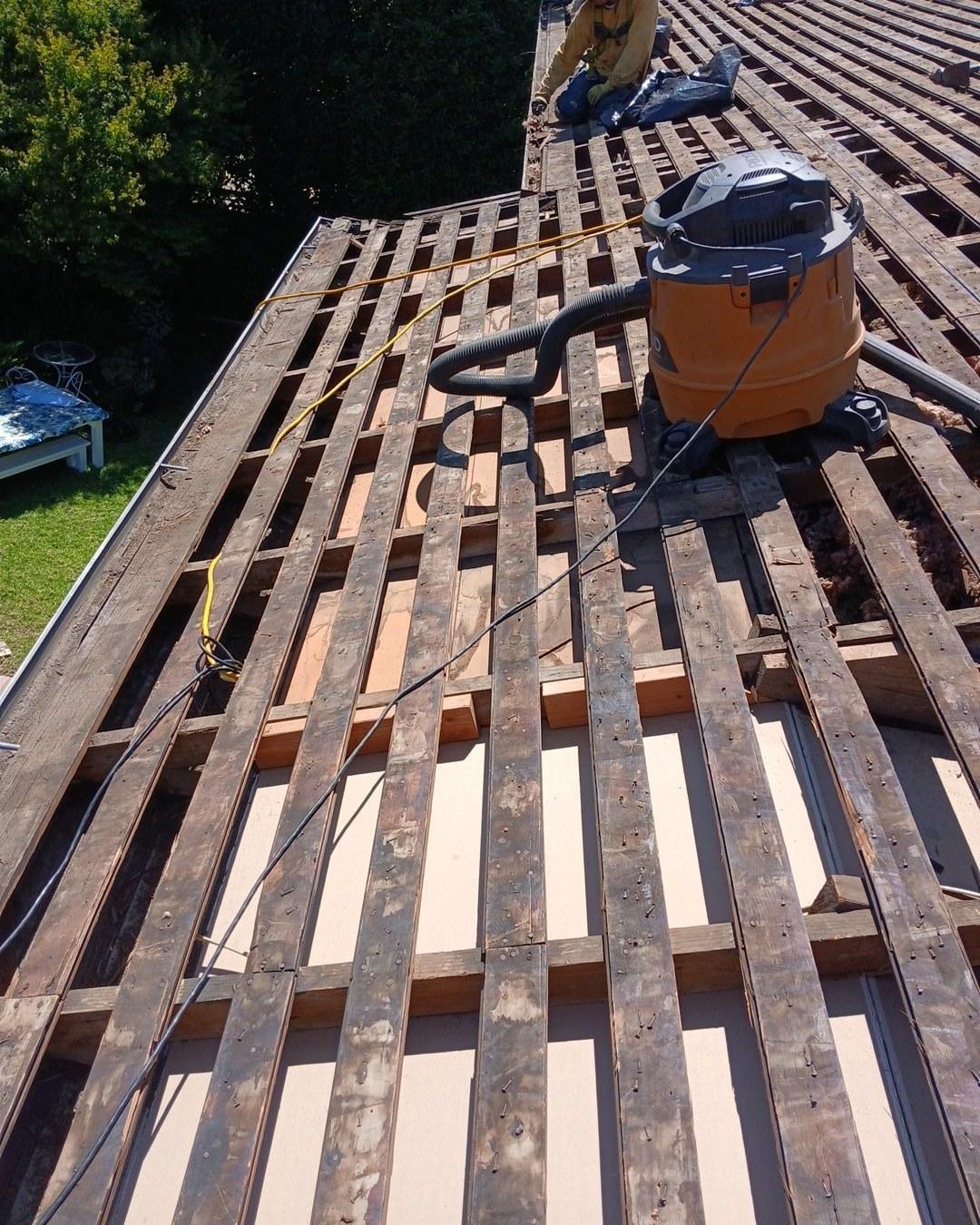 shingle-reroof-motor-ave-los-angeles-613 Roof tear-off exposing old spaced wood battens, orange shop vacuum and worker on rooftop during re-roofing project.