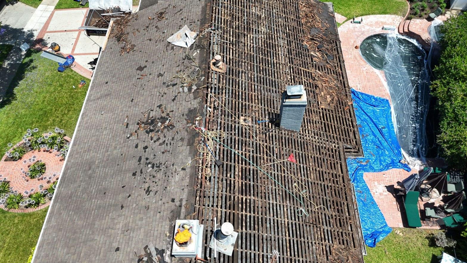 shingle-reroof-motor-ave-los-angeles-614 Aerial view of home roof mid-replacement, tiles removed exposing wood lath battens, blue tarps protecting pool area.