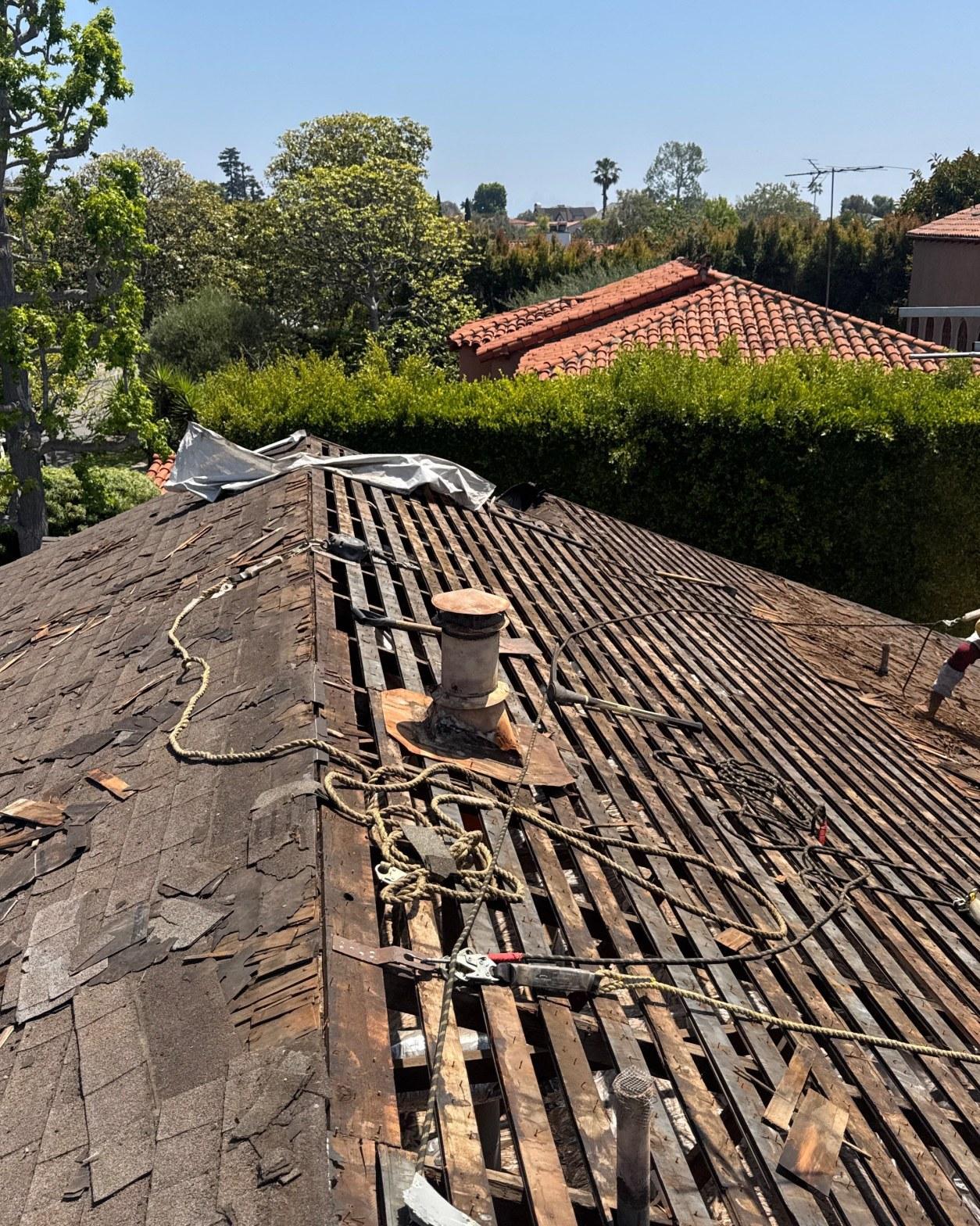 shingle-reroof-motor-ave-los-angeles-615 Roof tear-off showing exposed wooden lath strips, old vent pipe, and remaining asphalt shingles on residential home.