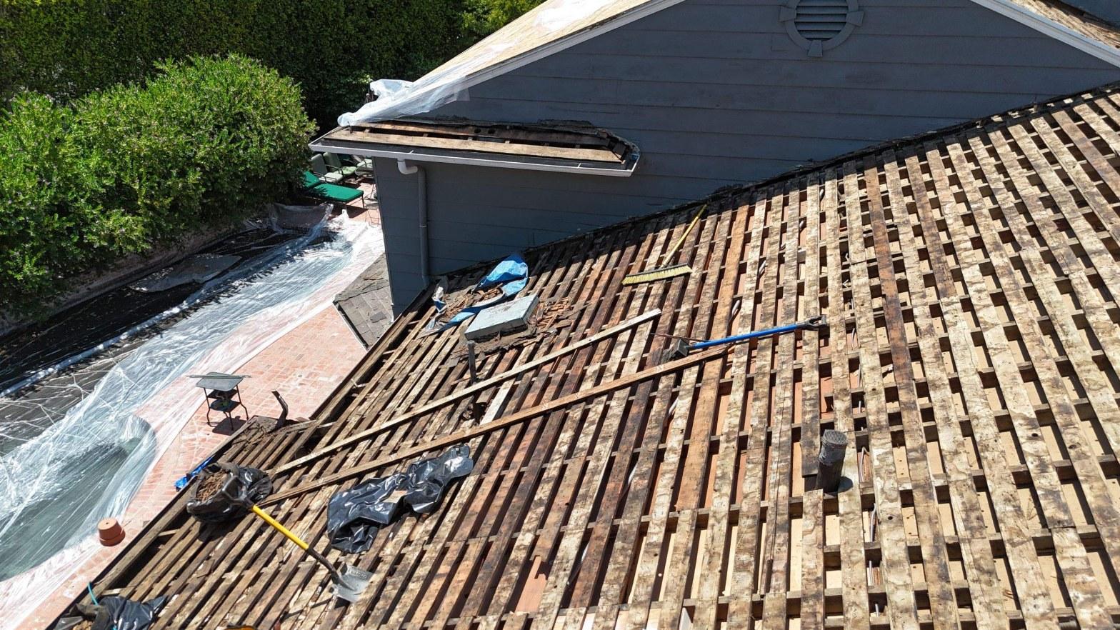 shingle-reroof-motor-ave-los-angeles-623 Aerial view of roof mid-renovation with tiles stripped, showing aged wood lath battens and debris on deck.