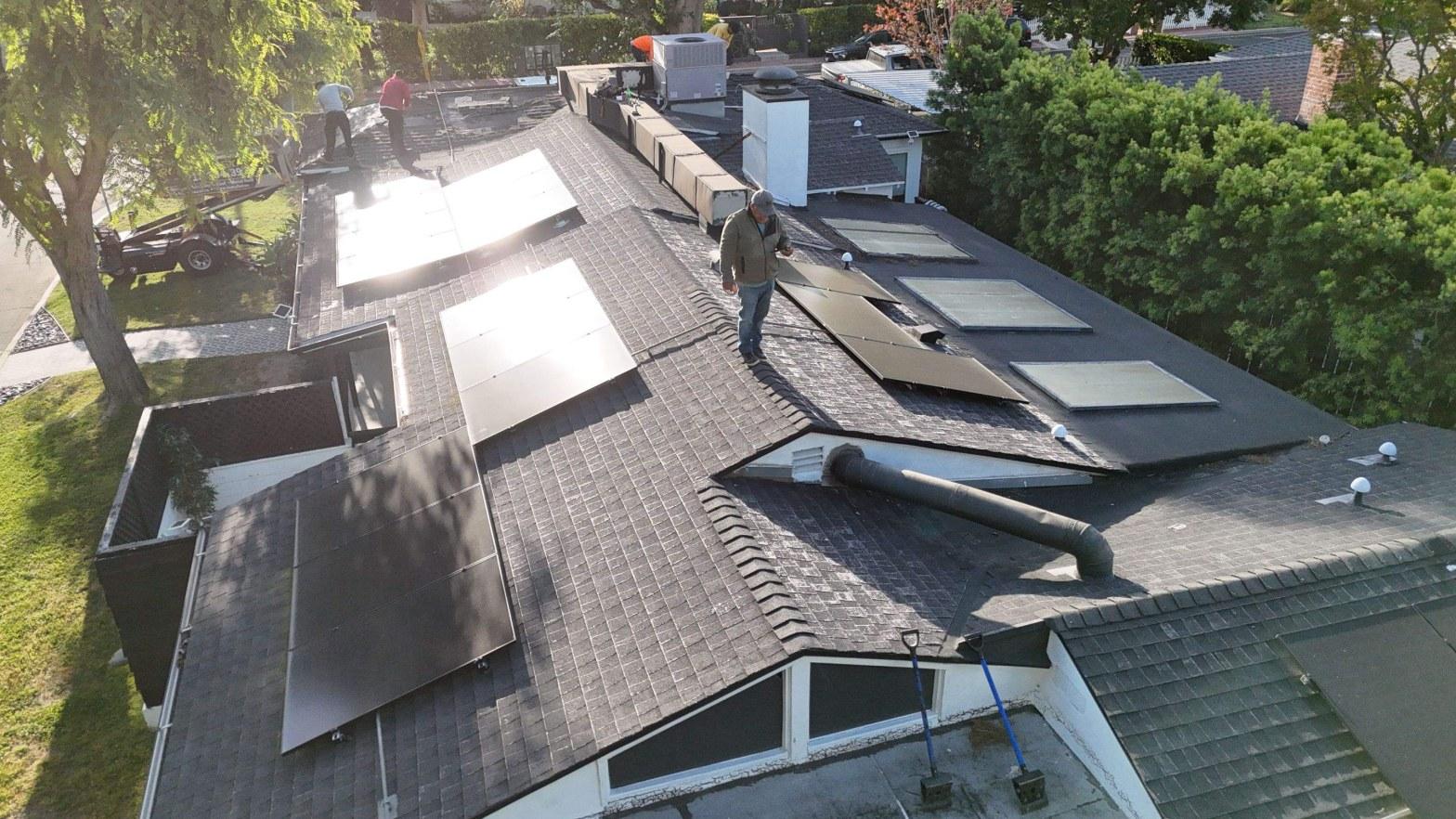 shingle-reroof-solar-complex-flashing-los-angeles-642 Aerial view of solar panel installation in progress on residential roof with skylights and HVAC units.
