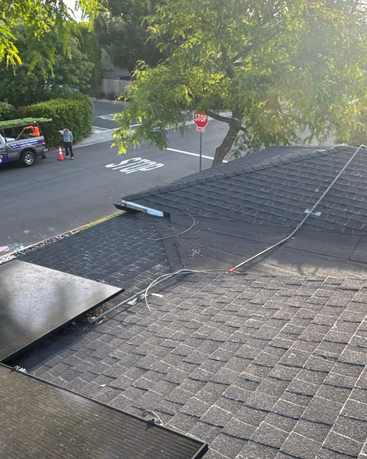shingle-reroof-solar-complex-flashing-los-angeles-645 Solar panel installation in progress on dark asphalt shingle roof with wiring visible, workers and truck in background.