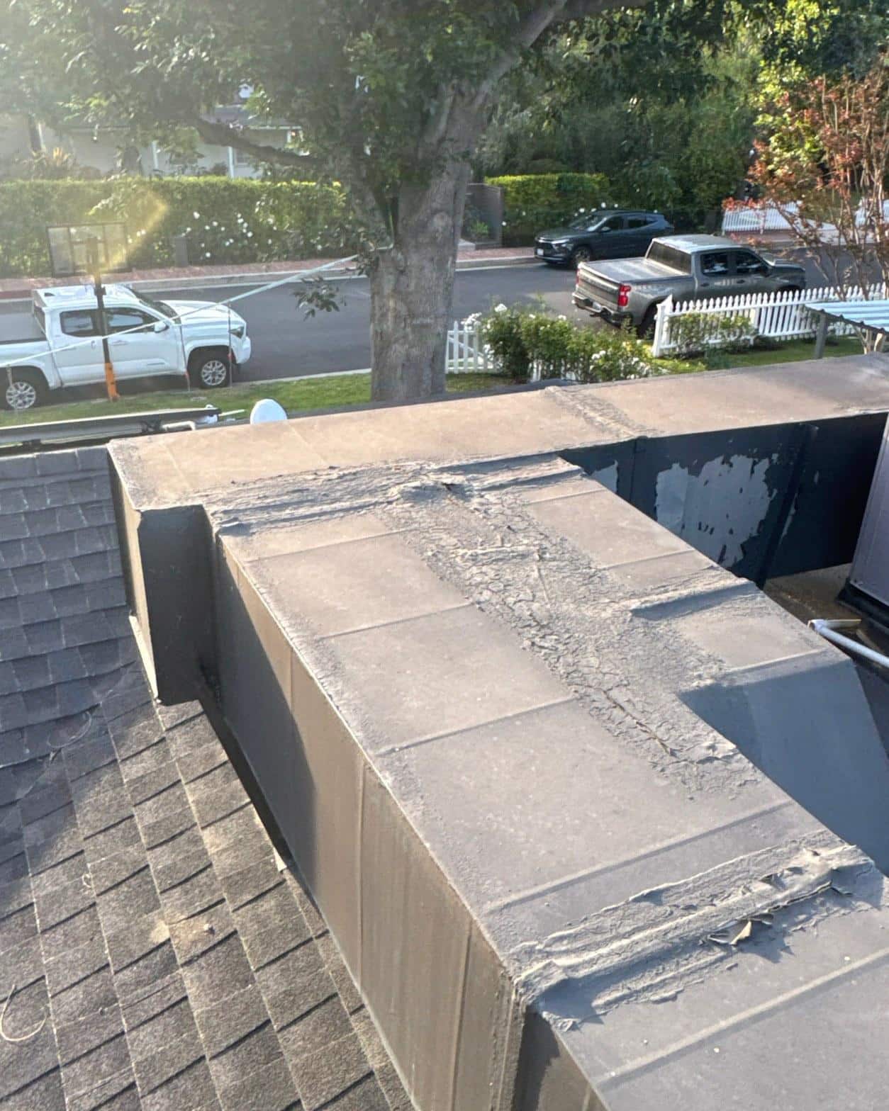 shingle-reroof-solar-complex-flashing-los-angeles-646 Damaged flat roof with cracked peeling membrane on parapet wall next to asphalt shingle slope, residential street visible below.