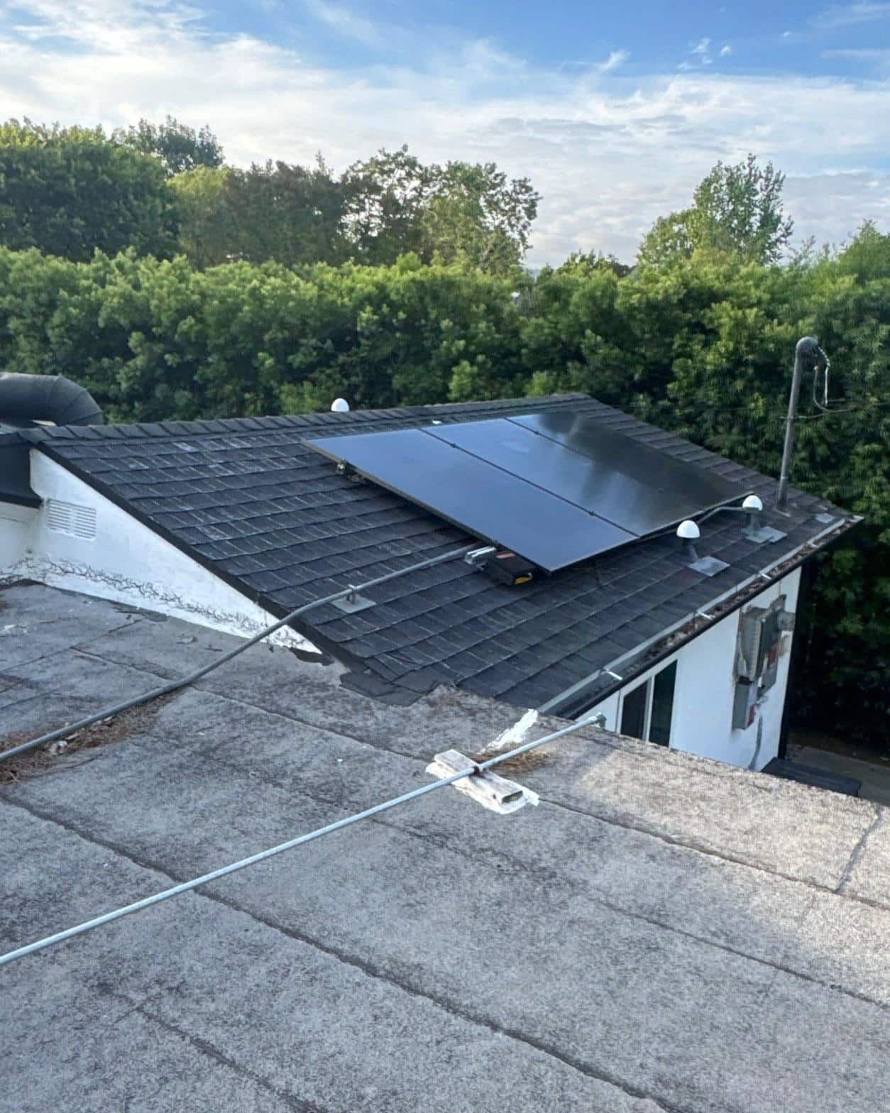 shingle-reroof-solar-complex-flashing-los-angeles-647 Four black monocrystalline solar panels installed on dark asphalt shingle roof with flat roof section in foreground.