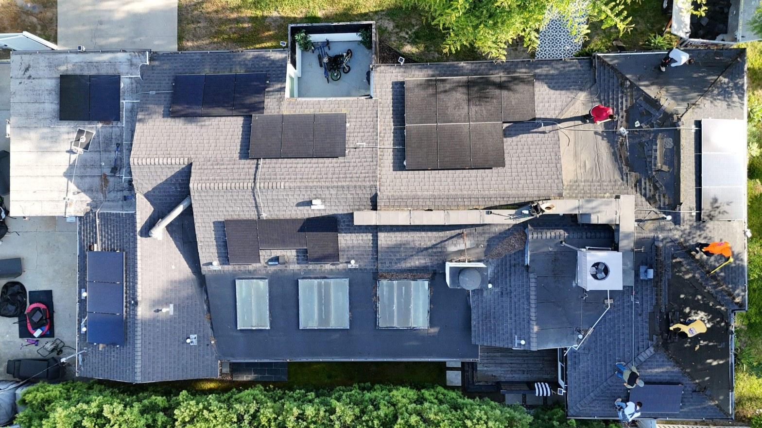 shingle-reroof-solar-complex-flashing-los-angeles-648 Drone aerial photo of residential rooftop with multiple solar panels installed and workers visible on roof.