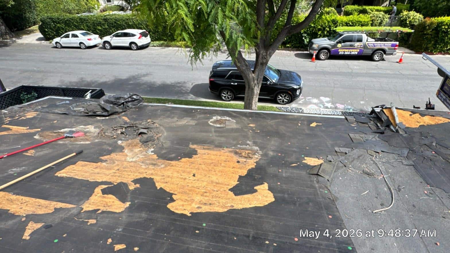 shingle-reroof-solar-complex-flashing-los-angeles-651 Roof tear-off in progress showing exposed OSB decking with water damage and torn underlayment, roofing truck visible on street.