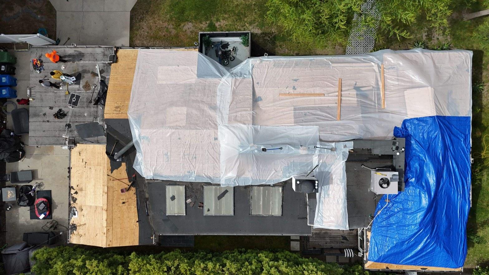 shingle-reroof-solar-complex-flashing-los-angeles-653 Aerial drone photo of residential roof replacement in progress, workers visible, white tarps and plywood decking exposed.