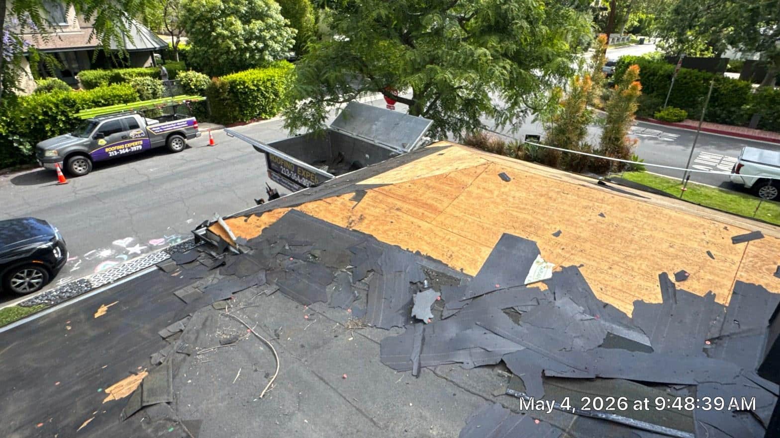 shingle-reroof-solar-complex-flashing-los-angeles-656 Roof tear-off in progress showing bare OSB decking with torn asphalt underlayment debris and dumpster on residential building.