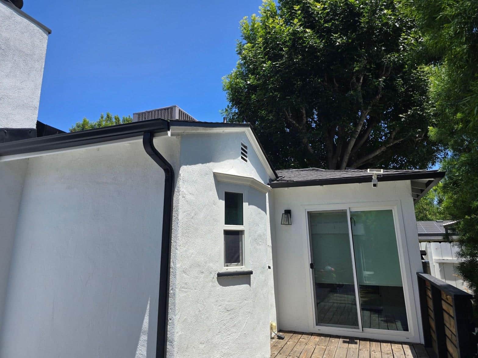 shingle-reroof-solar-complex-flashing-los-angeles-657 White stucco house exterior showing dark gutters, asphalt shingle roof, sliding glass door, and wood deck.