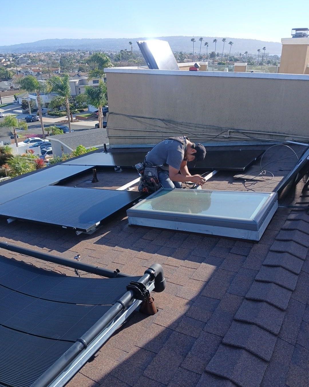 Technician securing solar panel wiring on newly reroofed Redondo Beach home with large skylight visible nearby