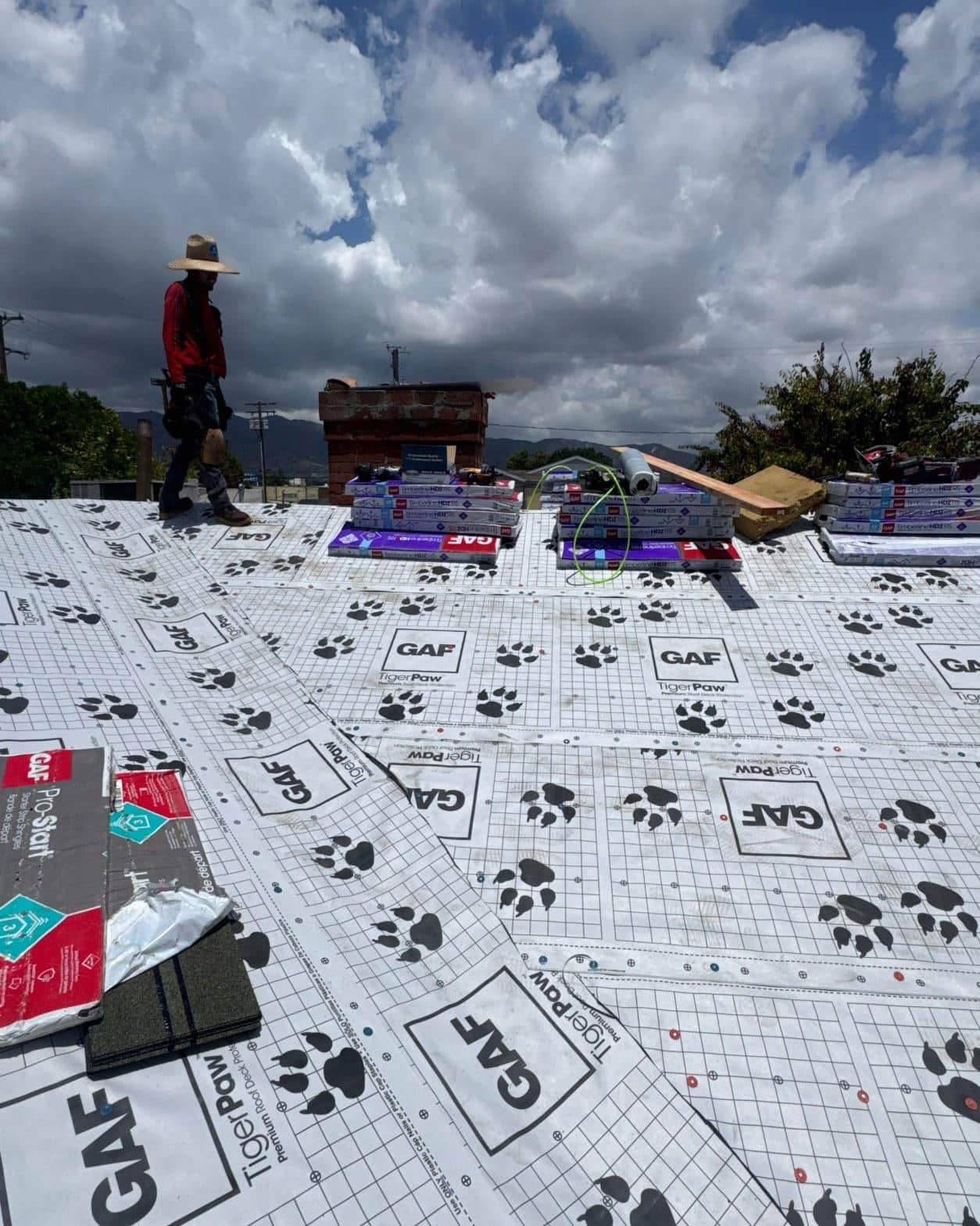 single-reroof-burbank-ca-shingles-flat-flashing-574 Roofer in straw hat walking on GAF TigerPaw roof underlayment with shingle bundles stacked nearby.