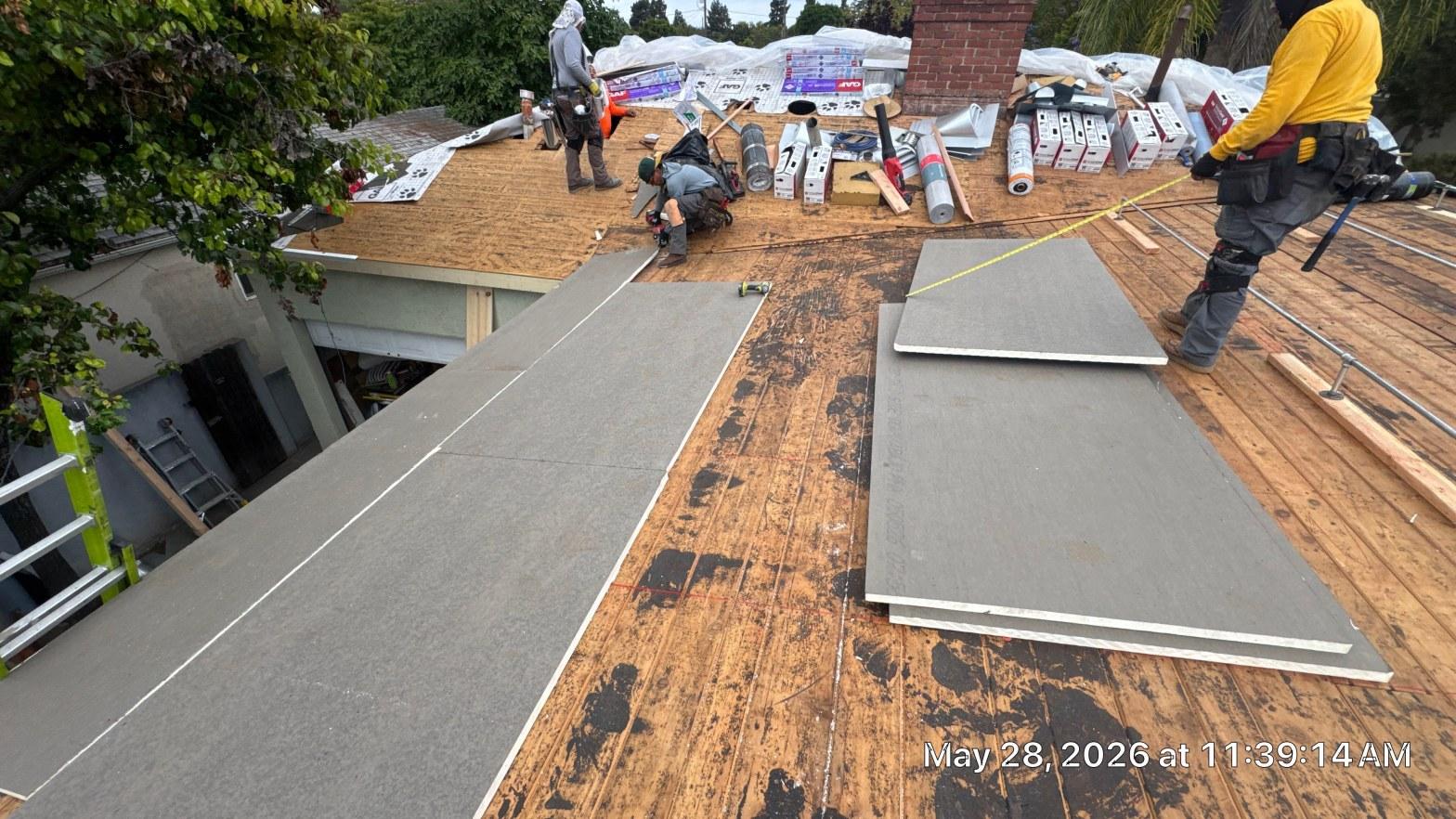 single-reroof-burbank-ca-shingles-flat-flashing-576 Roofing crew laying gray underlayment sheets on bare wood decking during residential roof replacement.