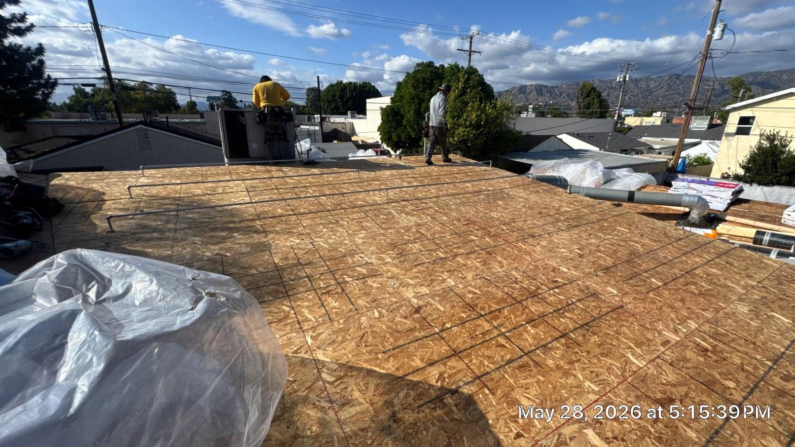 single-reroof-burbank-ca-shingles-flat-flashing-581 Two roofers standing on flat roof covered with new OSB plywood decking, mountains visible in background.