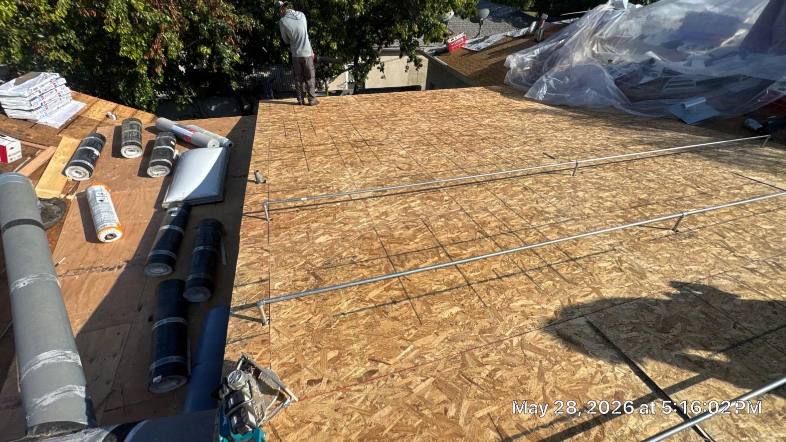 single-reroof-burbank-ca-shingles-flat-flashing-582 New OSB roof sheathing on flat roof with rolled underlayment, safety rails, and roofer working in background.