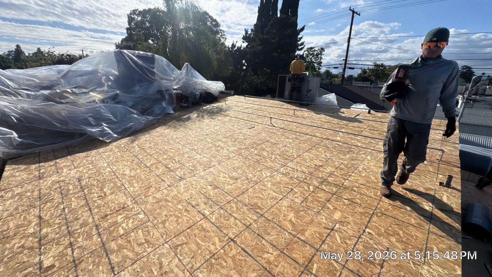 single-reroof-burbank-ca-shingles-flat-flashing-583 Roofers walking on newly installed OSB plywood decking on flat commercial roof, materials covered with plastic sheeting.