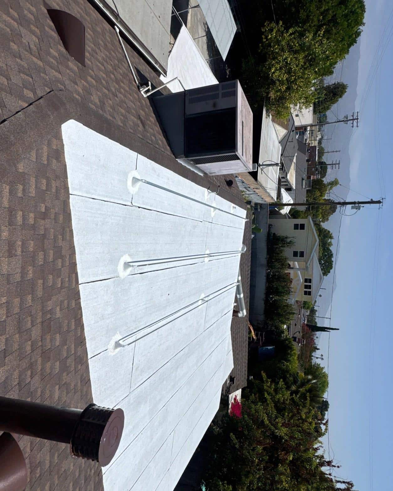single-reroof-burbank-ca-shingles-flat-flashing-585 White TPO membrane flat roof with pipe penetrations and boots beside brown asphalt shingle pitched roof, HVAC unit visible.
