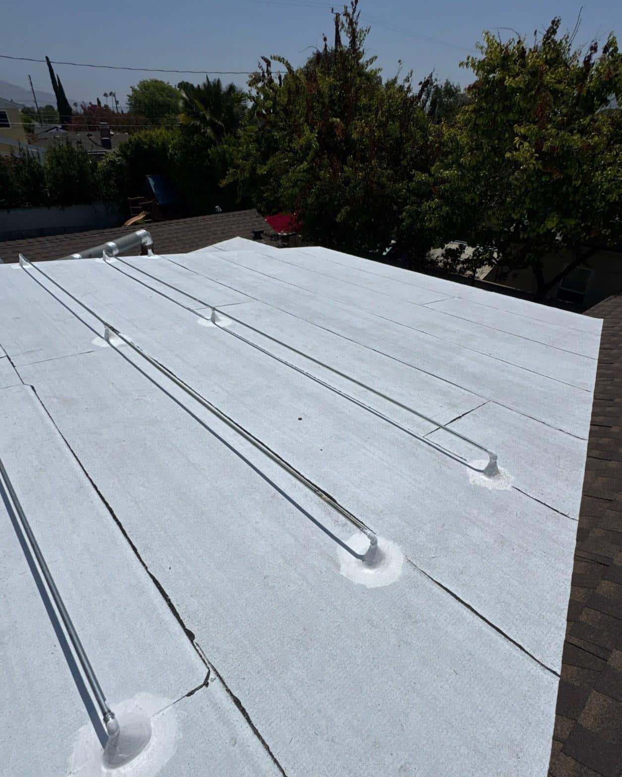 single-reroof-burbank-ca-shingles-flat-flashing-589 White membrane flat roof with visible seams, metal conduit lines, and pipe penetrations on residential building.