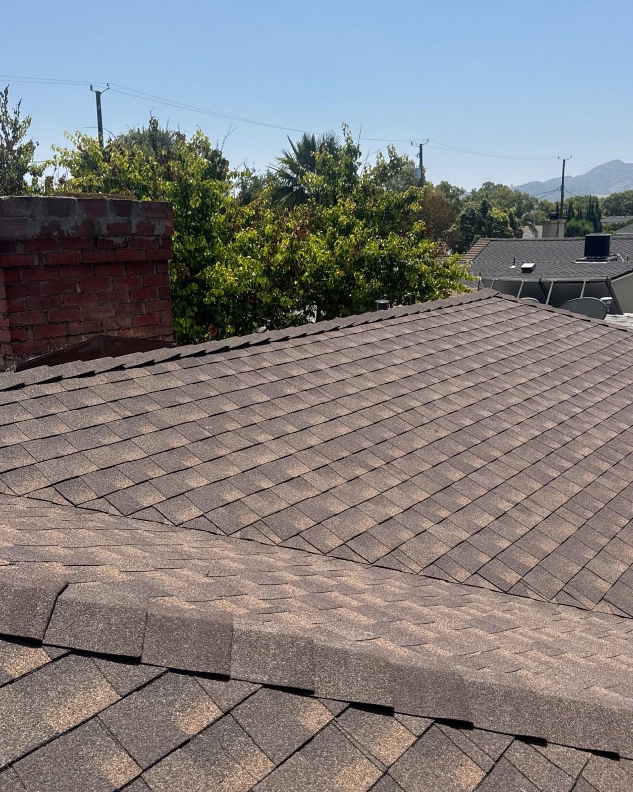 single-reroof-burbank-ca-shingles-flat-flashing-592 Newly installed brown asphalt shingle roof with weathered brick chimney, trees and mountains in background.