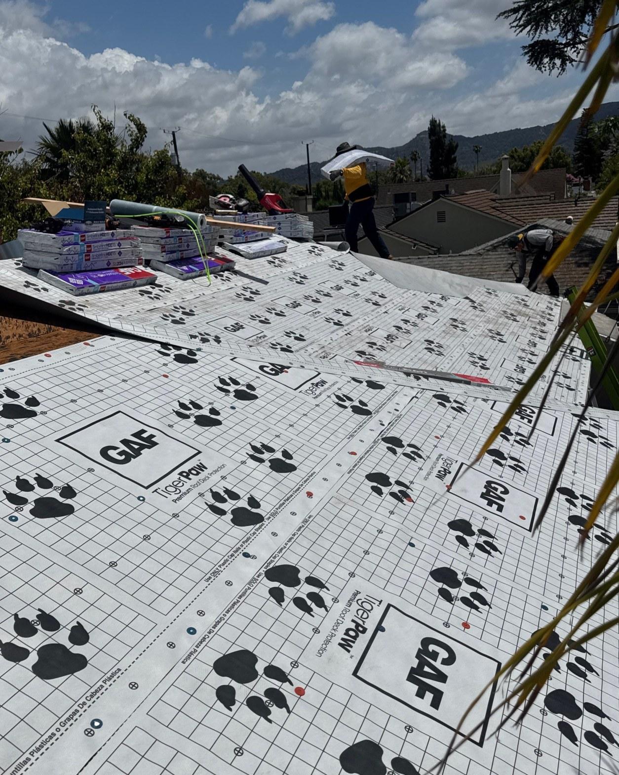single-reroof-burbank-ca-shingles-flat-flashing-596 GAF TigerPaw premium roof deck protection underlayment being installed on residential roof with workers and shingle bundles visible.
