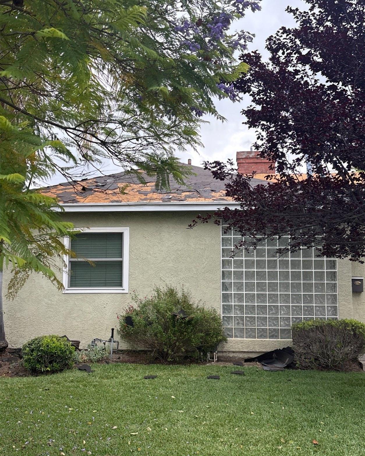 Storm-damaged Burbank home with asphalt shingles blown off roof, exposing OSB wood decking across multiple sections
