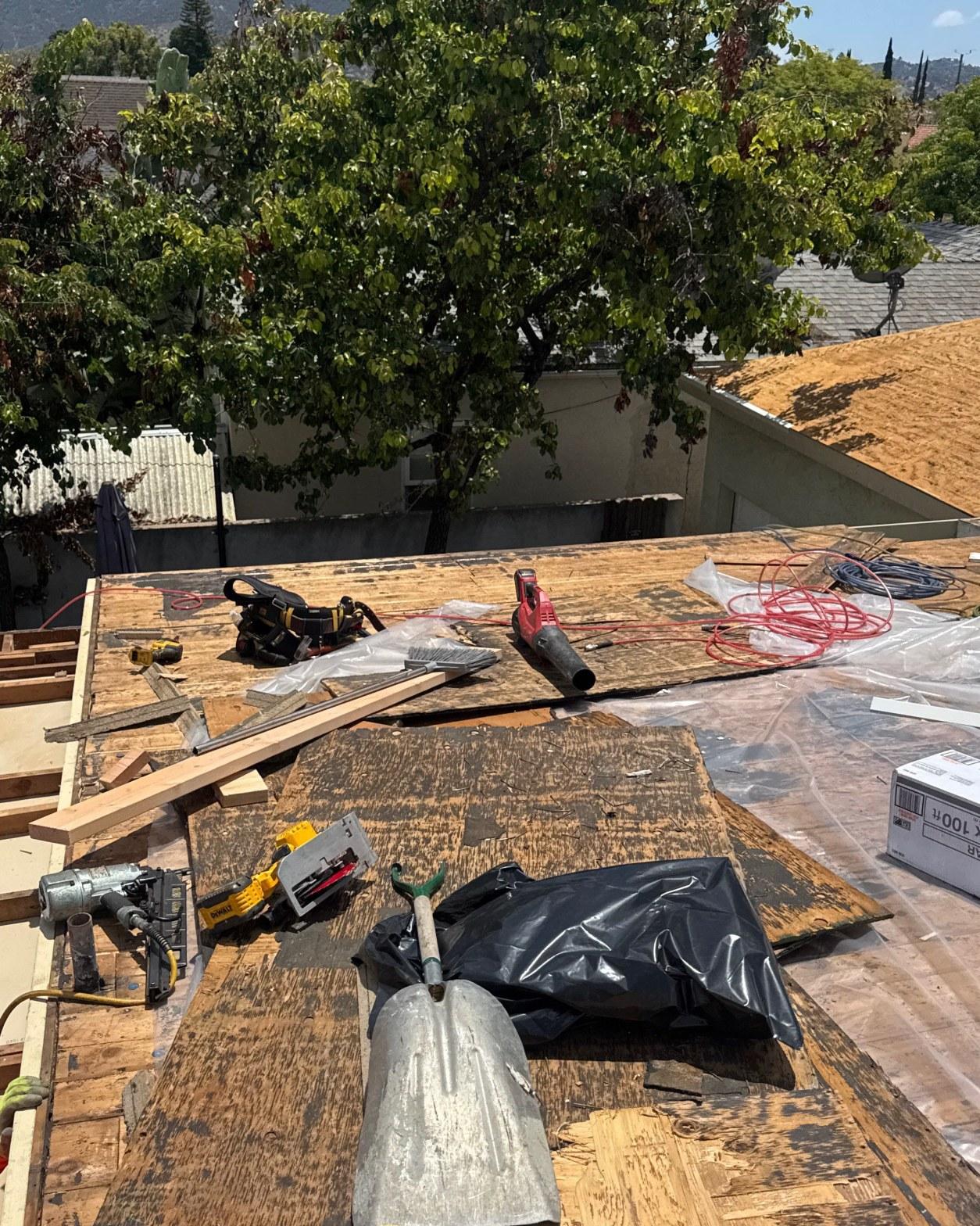 single-reroof-burbank-ca-shingles-flat-flashing-599 Residential roof tear-off exposing plywood decking with DeWalt saw, nail gun, leaf blower, and lumber debris on flat roof.
