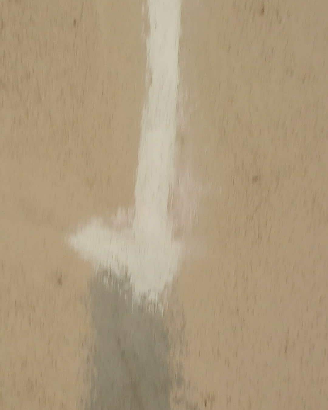 Blurry close-up of white caulk or filler applied to a vertical crack in a tan wall surface.