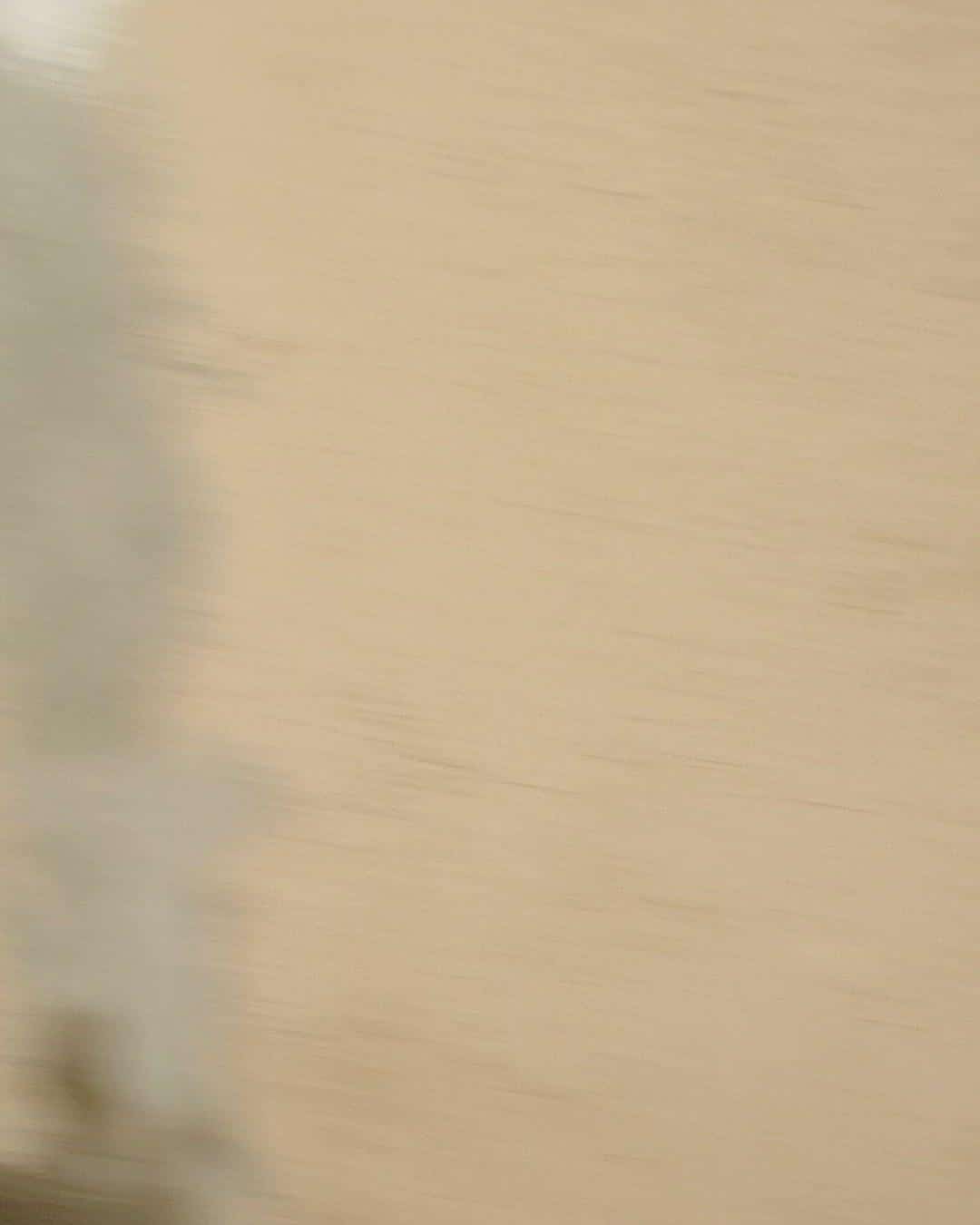 Out-of-focus motion-blurred beige wall surface with diagonal light and shadow patterns.