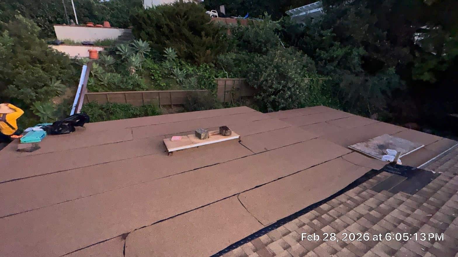 Brown mineral-surface flat roof membrane installed on residential home, worker and tools visible on left edge.
