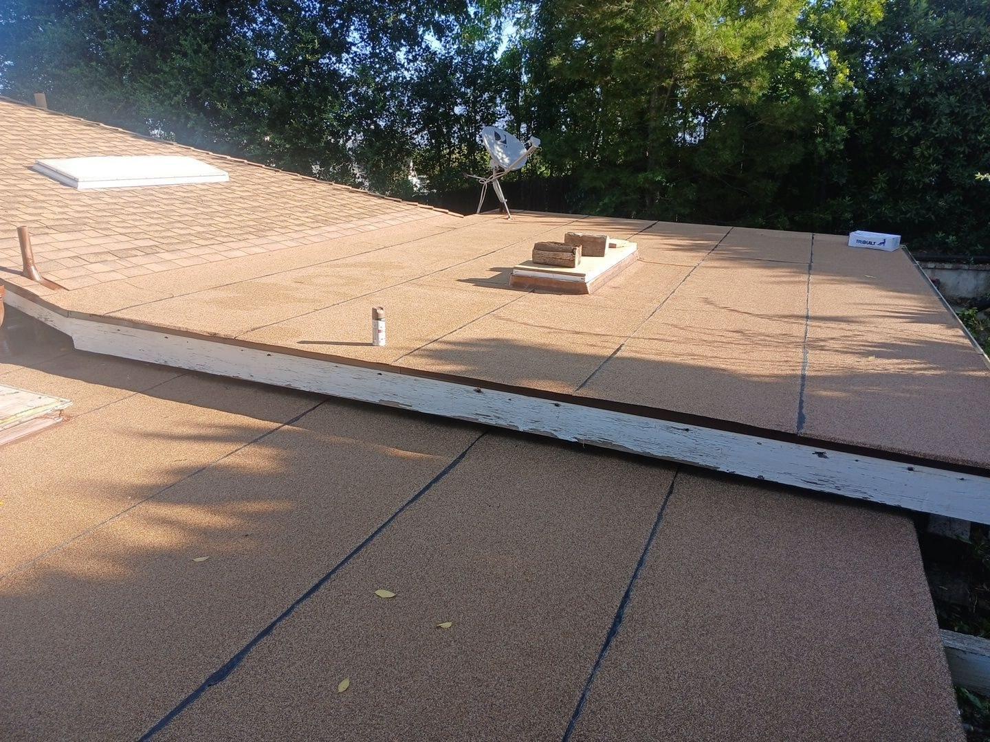 Newly installed tan granulated flat roof membrane with seams, wood parapet edge, skylight curb, and satellite dish visible.