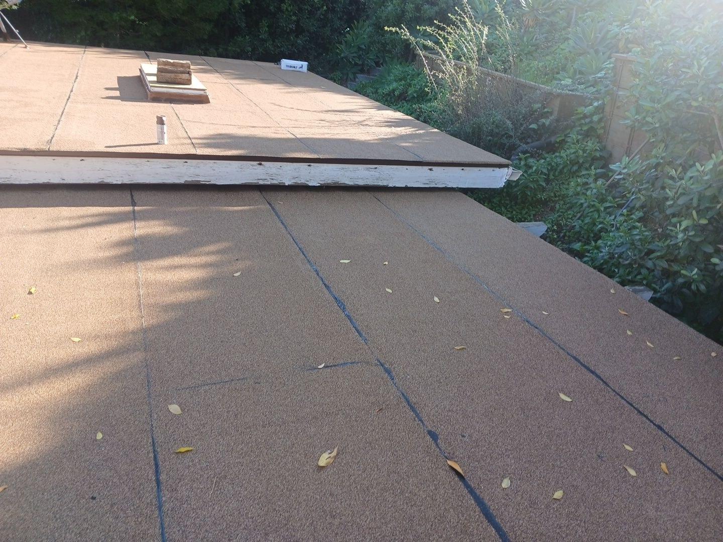 Freshly installed tan mineral-surface rolled roofing on flat roof with raised section and white fascia trim visible.
