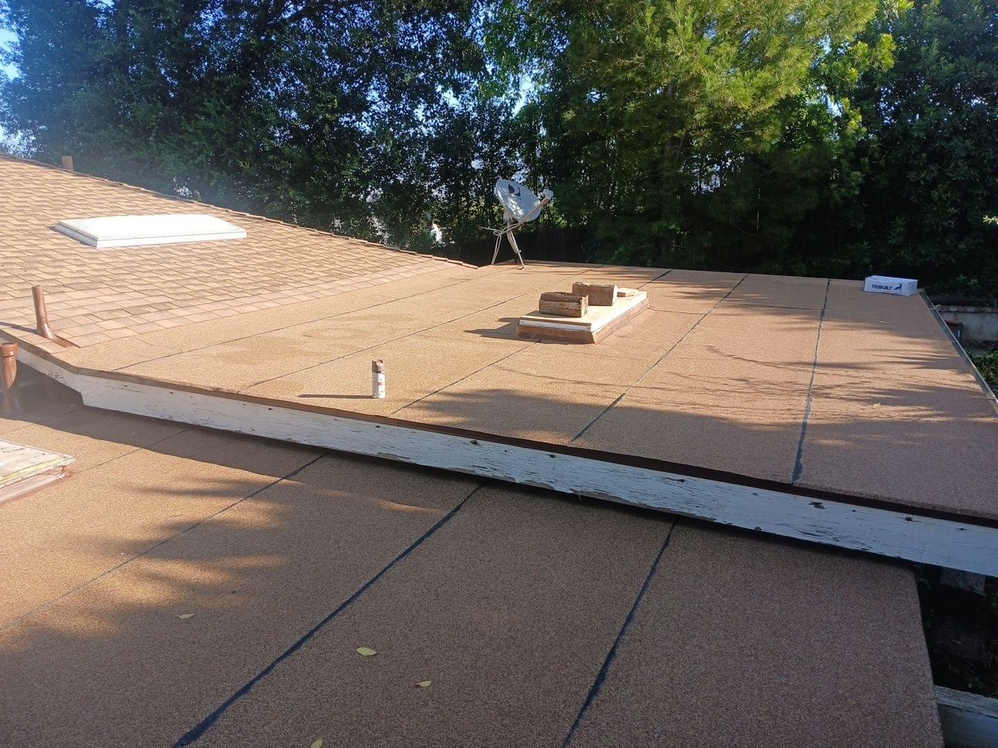 Flat roof covered in brown mineral-surface felt sheets with skylight opening, satellite dish, and TruBuilt materials visible.