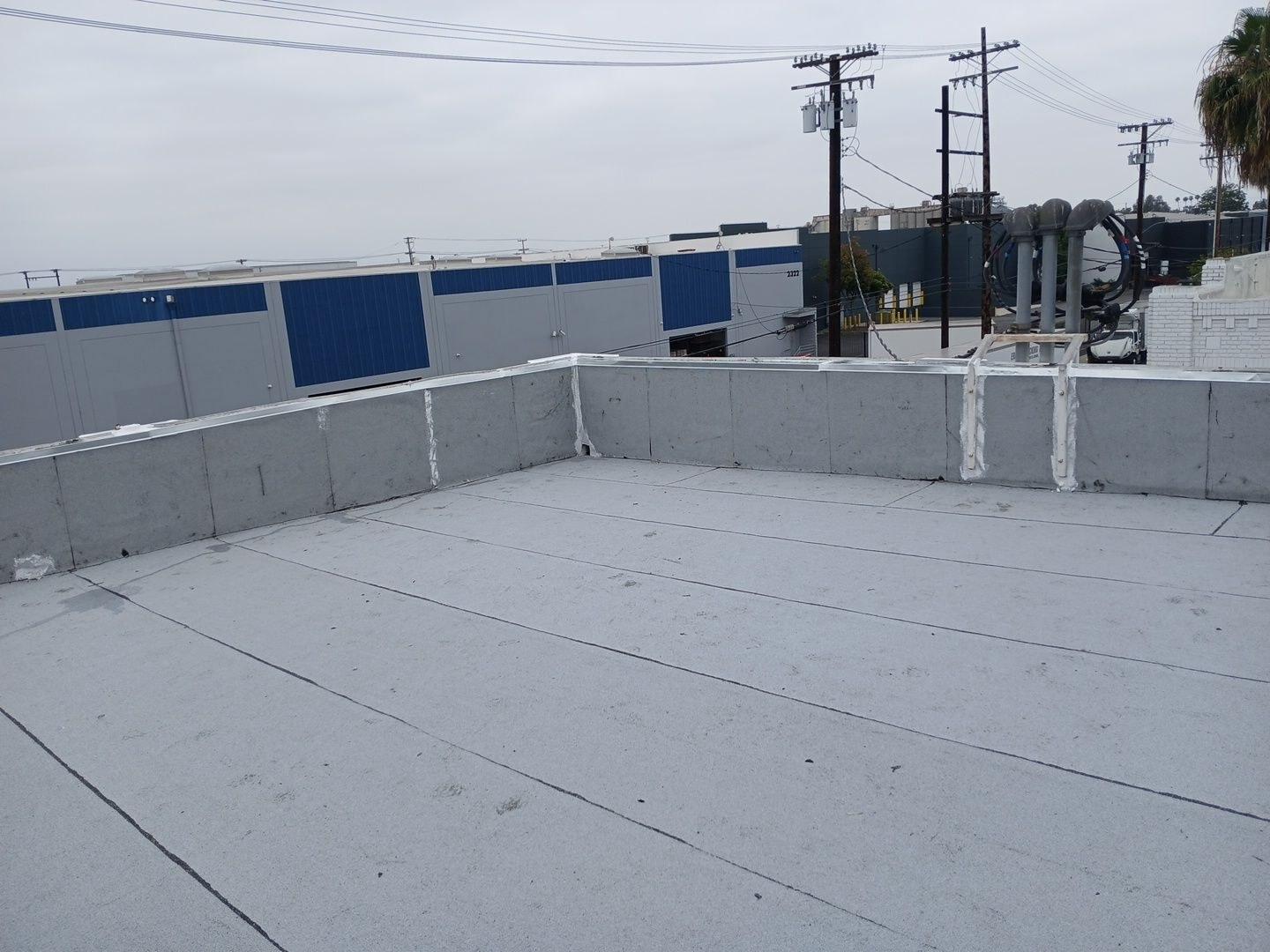 White elastomeric coating applied to flat commercial rooftop with concrete parapet walls and utility poles in background.
