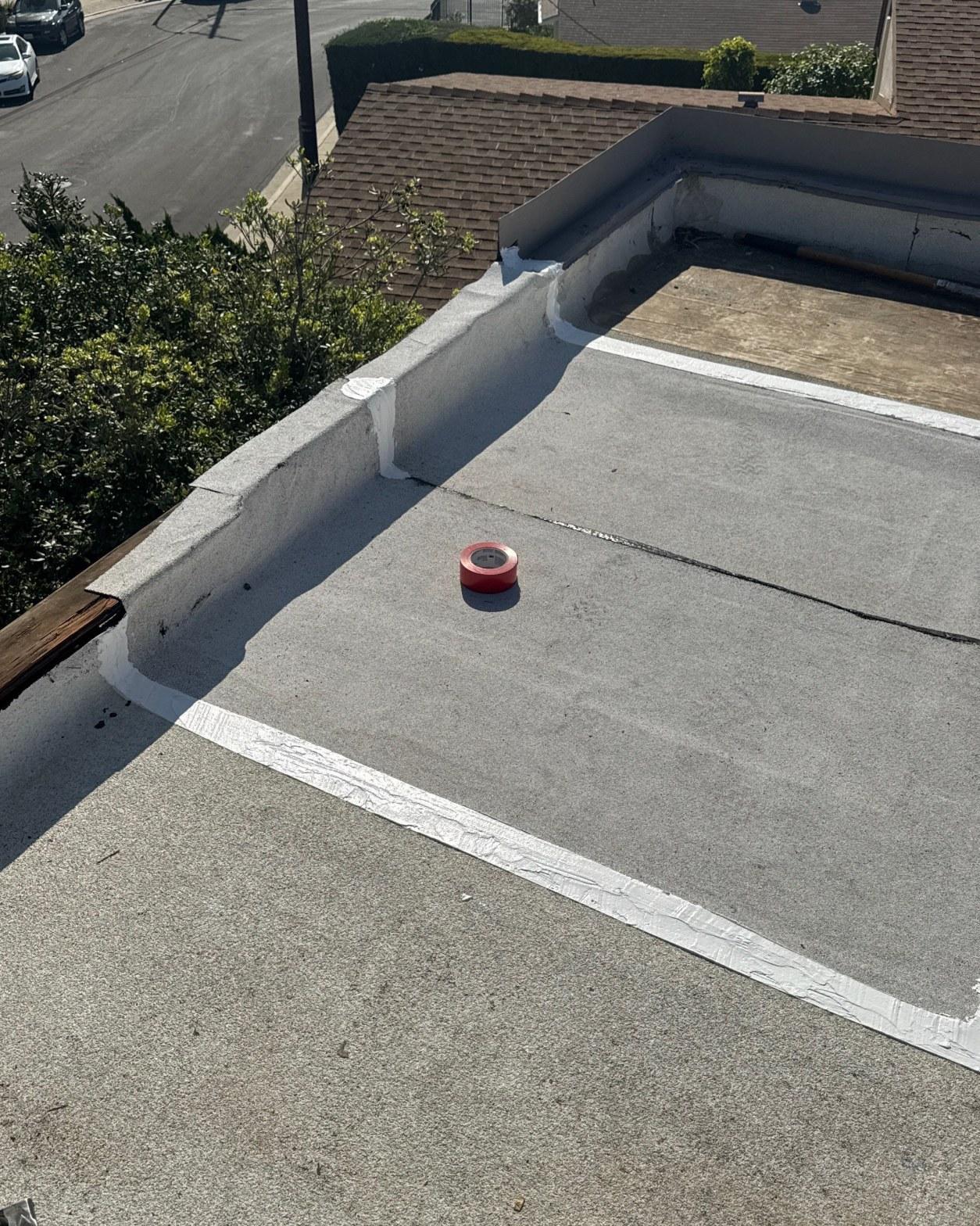 Roll of red seam tape on flat gravel roof surface during torch down repair, Los Angeles CA 90042