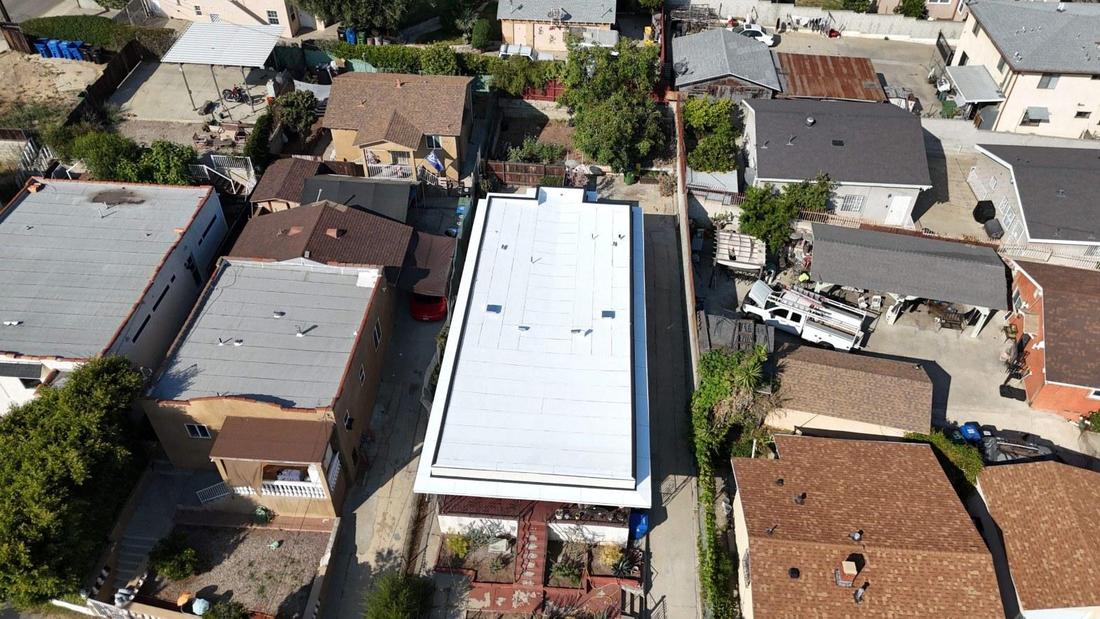 Aerial view of newly installed white TPO or PVC flat roof membrane on residential building surrounded by neighborhood homes.