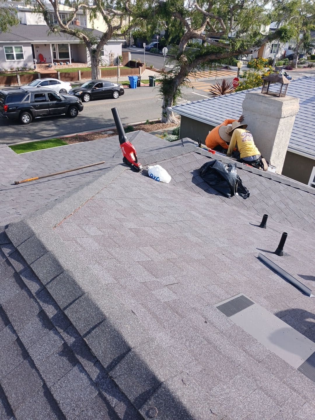 Roofers flashing chimney on new asphalt shingle roof, blower and pipe boots visible — Roof Replacement Inc