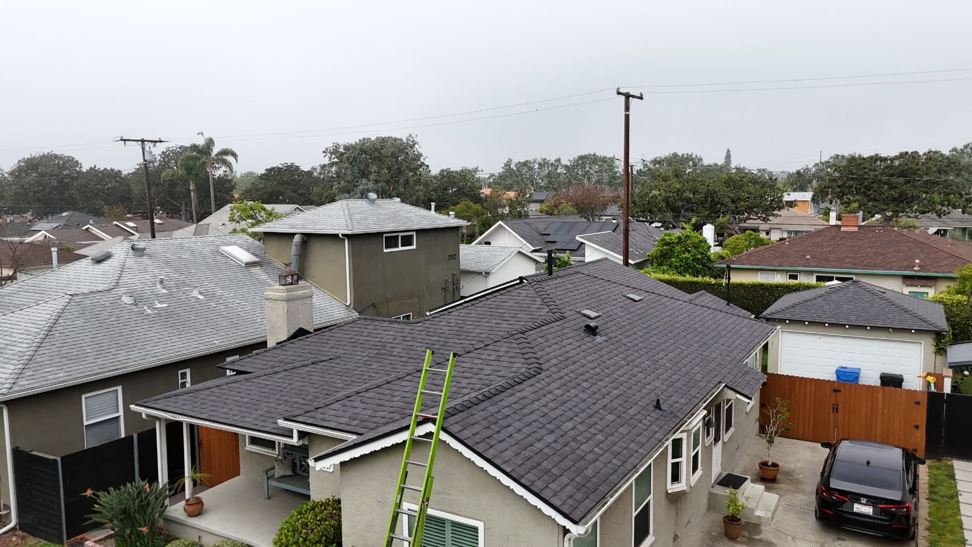 Completed dark asphalt shingle hip roof, green ladder leaning on eave | Roof Replacement Inc Completed dark asphalt shingle hip roof, green ladder leaning on eave — Roof Replacement Inc