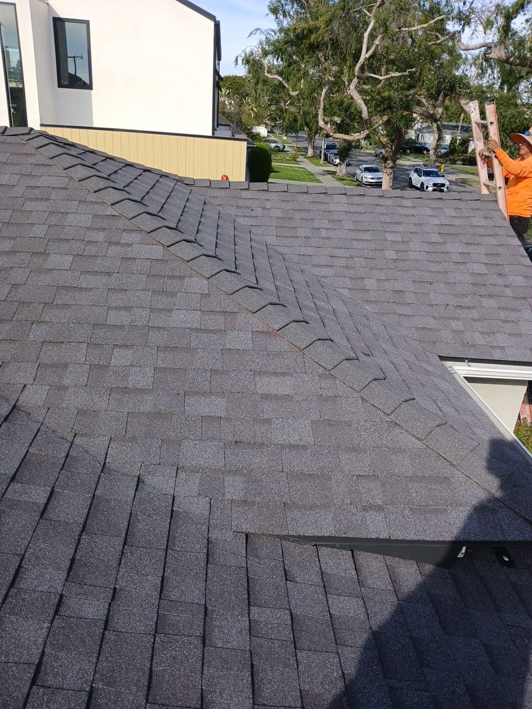 Gray asphalt shingle roof with hip valleys; worker climbing ladder | Roof Replacement Inc Gray asphalt shingle roof with hip valleys; worker climbing ladder — Roof Replacement Inc