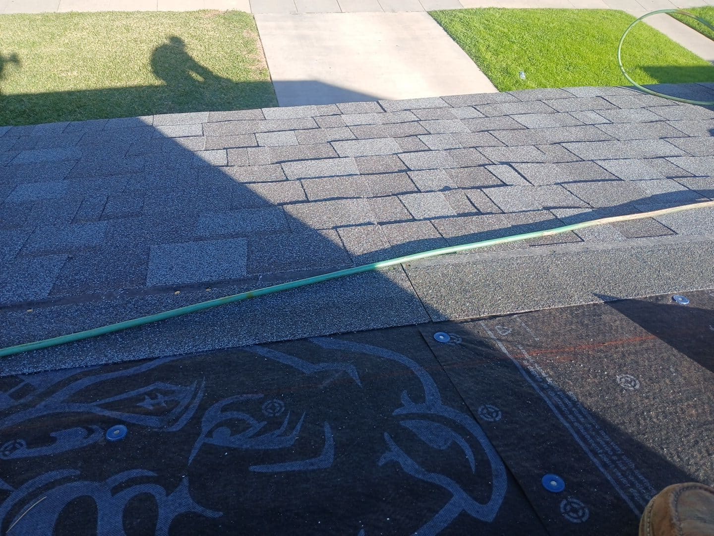 Gray asphalt shingles being installed over black underlayment with green hose | Roof Replacement Inc Gray asphalt shingles being installed over black underlayment with green hose — Roof Replacement Inc