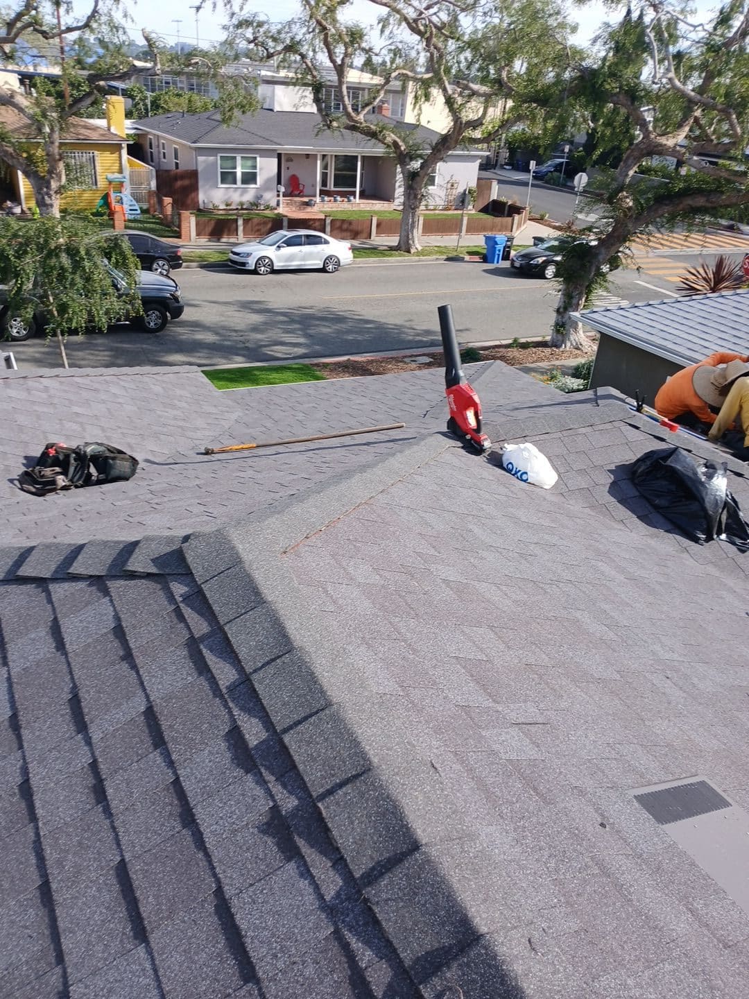 Asphalt shingle re-roof with nail gun, pipe boot, worker at ridge — Roof Replacement Inc