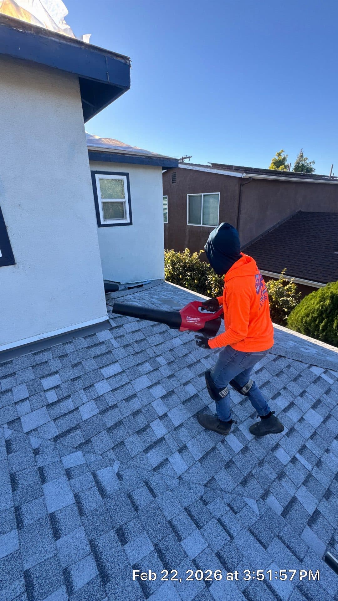 Worker blowing debris off new asphalt shingle roof with Milwaukee blower | Roof Replacement Inc Worker blowing debris off new asphalt shingle roof with Milwaukee blower — Roof Replacement Inc