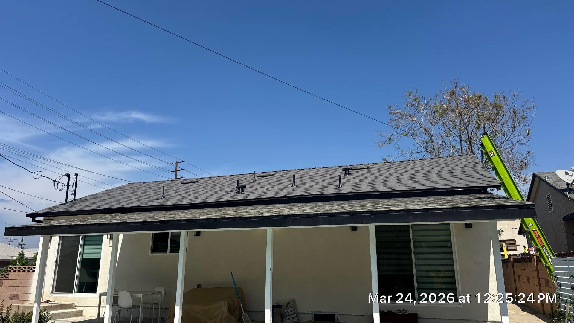 Completed asphalt shingle roof with pipe boots, fascia, green ladder leaning on eave | Roof Replacement Inc Completed asphalt shingle roof with pipe boots, fascia, green ladder leaning on eave — Roof Replacement Inc