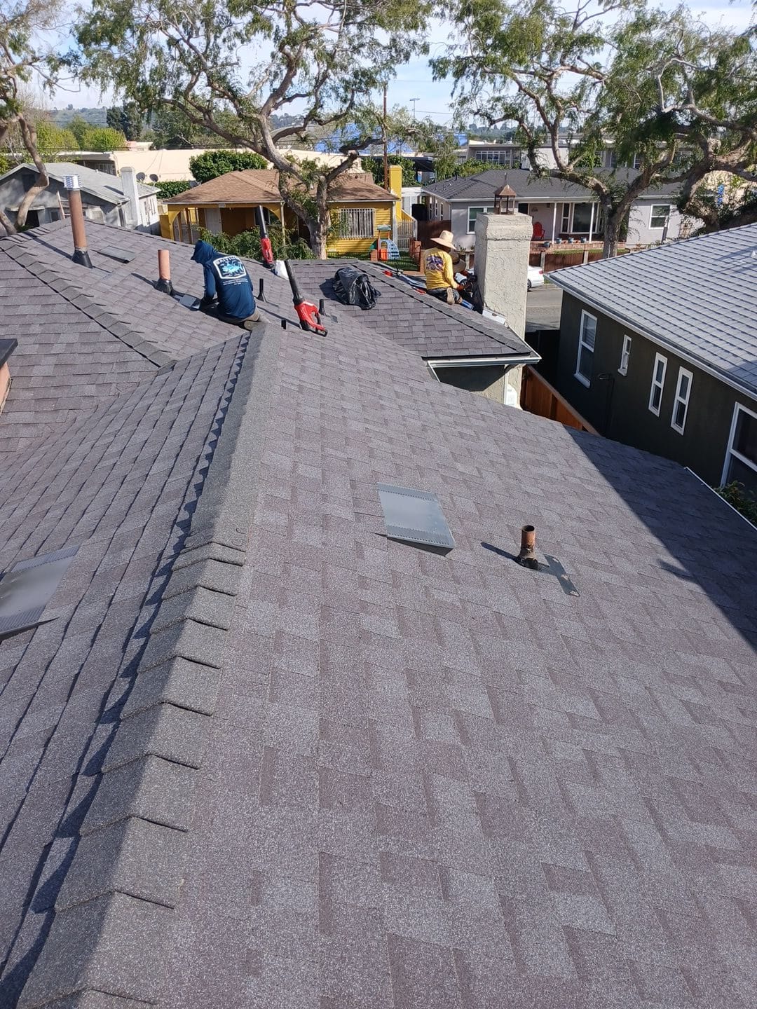 Crew installing gray asphalt shingles on large residential roof with chimney | Roof Replacement Inc Crew installing gray asphalt shingles on large residential roof with chimney — Roof Replacement Inc