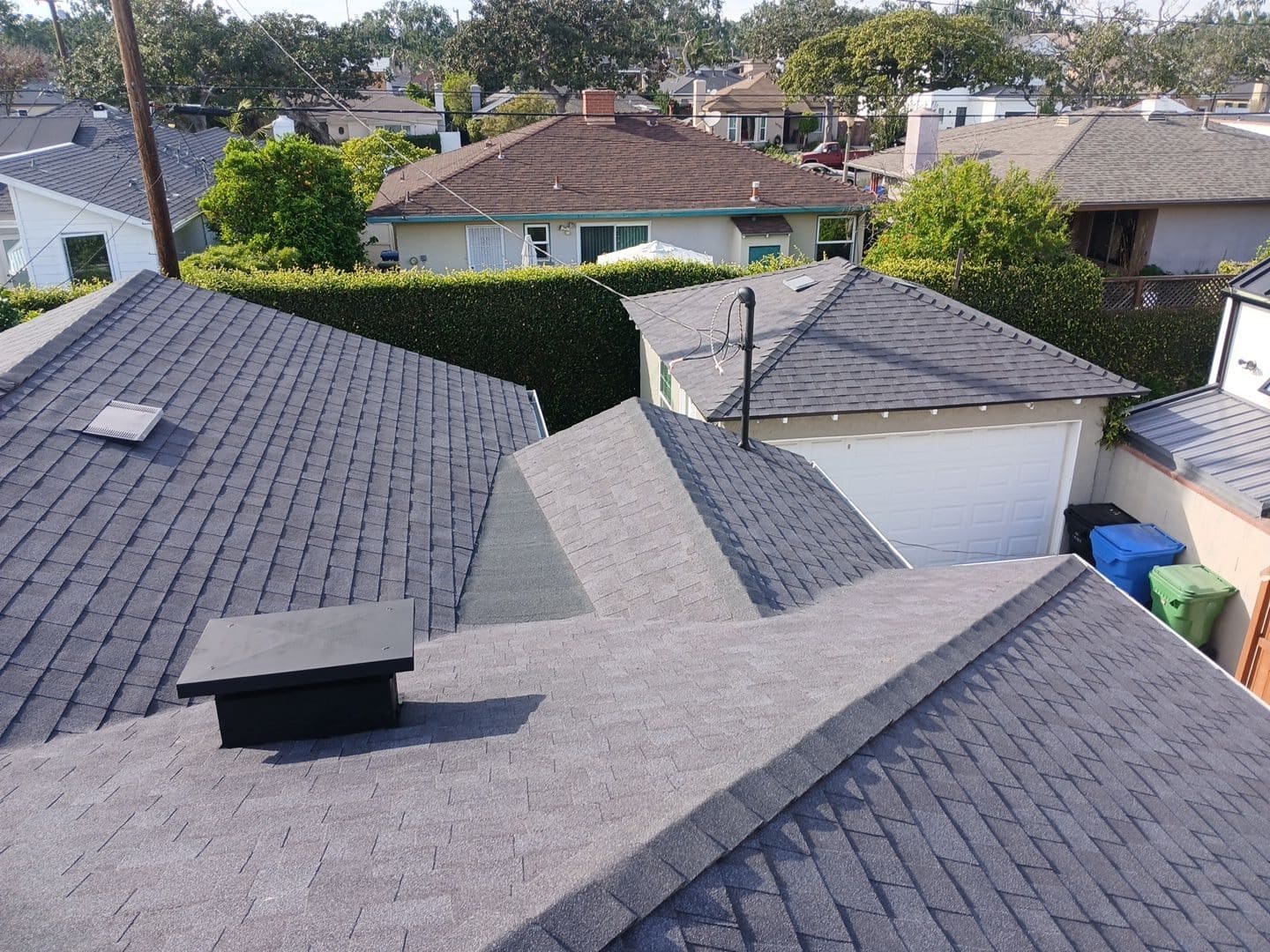 Gray asphalt shingle roof with chimney cap, vent pipe, skylight, and garage below. — Roof Replacement Inc