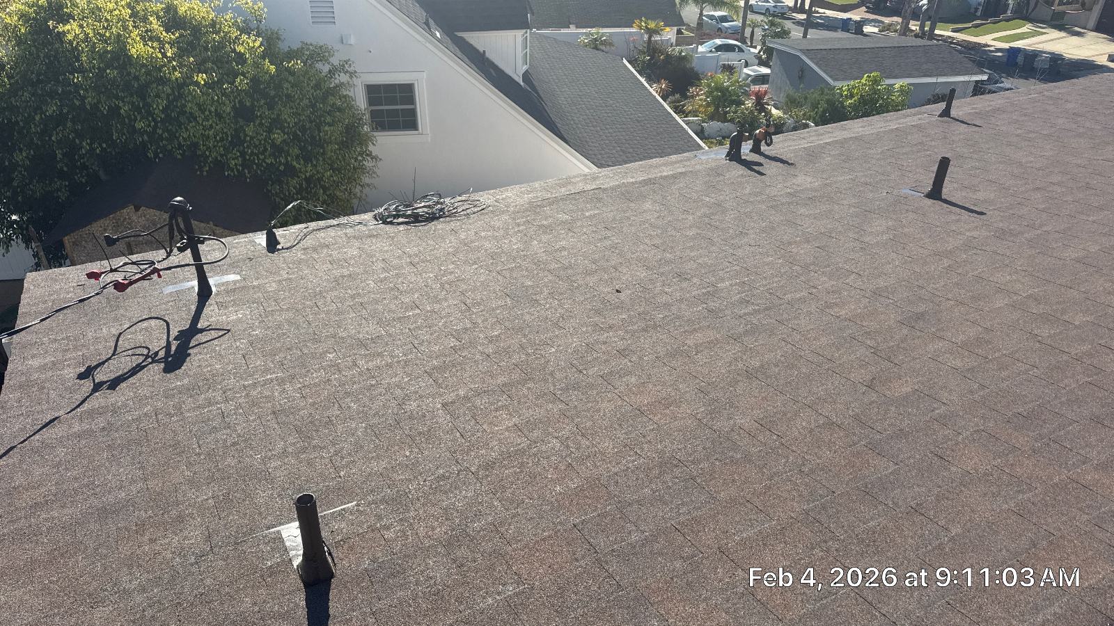Asphalt shingle roof with pipe boots, tools, and coiled wiring on slope — Roof Replacement Inc